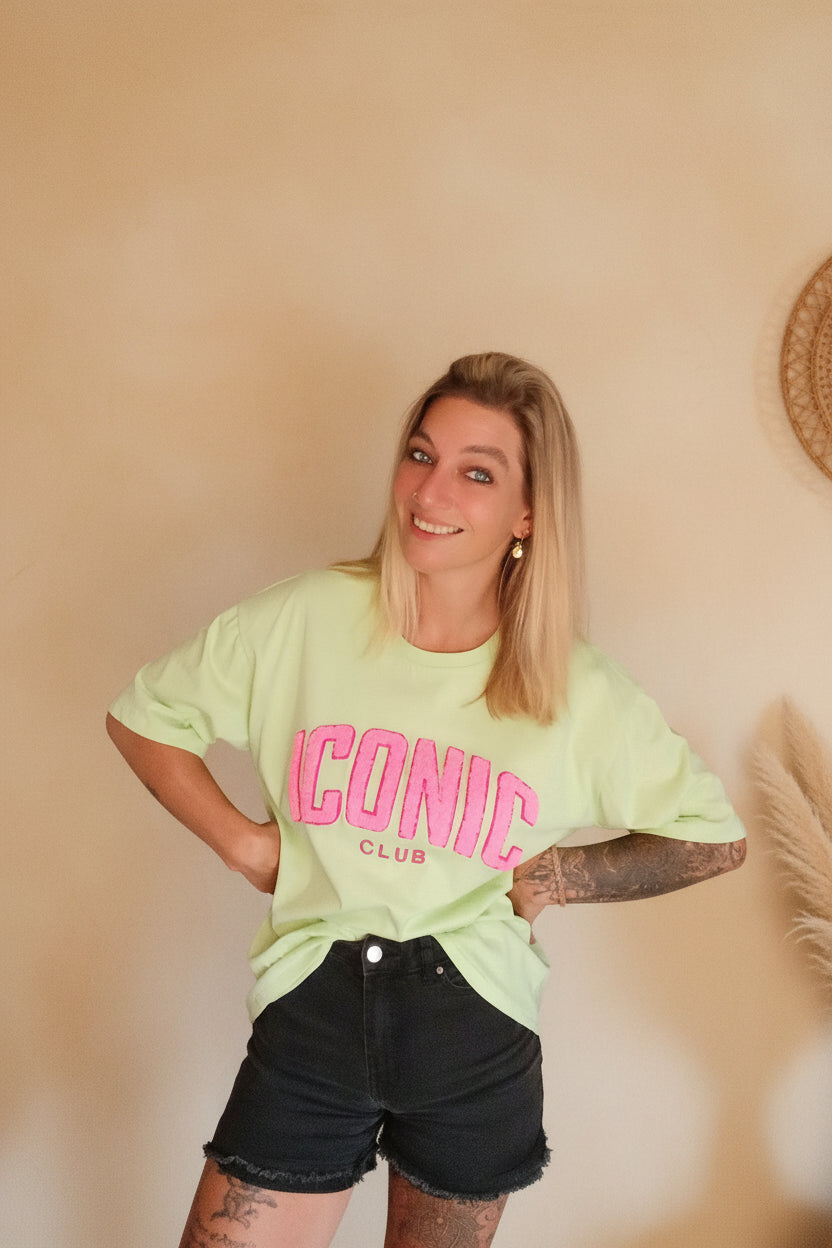 Iconic Club Oversized T-Shirt Salbeigrün – Frontansicht lächelnd, warmer Boho-Hintergrund