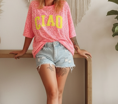 Boho-Luxe Look: Rosa gemustertes T-Shirt mit gelbem CIAO-Schriftzug und hellblaue Denim-Shorts.