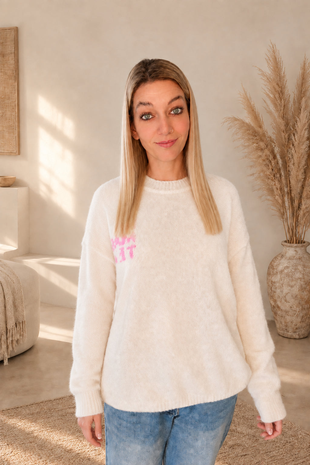 Vorderansicht des cremeweißen Strickpullovers mit kleinem rosa Namasté-Brustprint, am Model mit blauer Jeans.