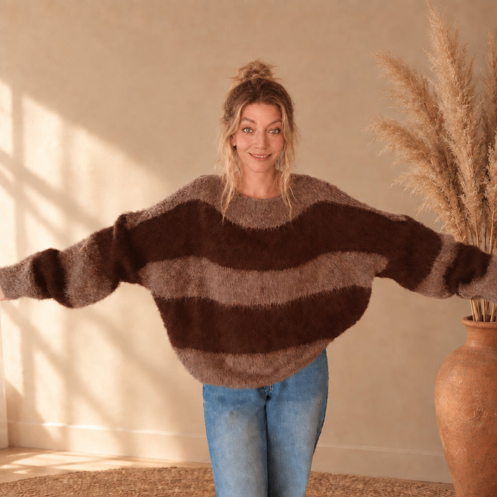 Model zeigt die weite Passform und die Ärmel des braun-taupe gestreiften Pullovers mit ausgestreckten Armen.