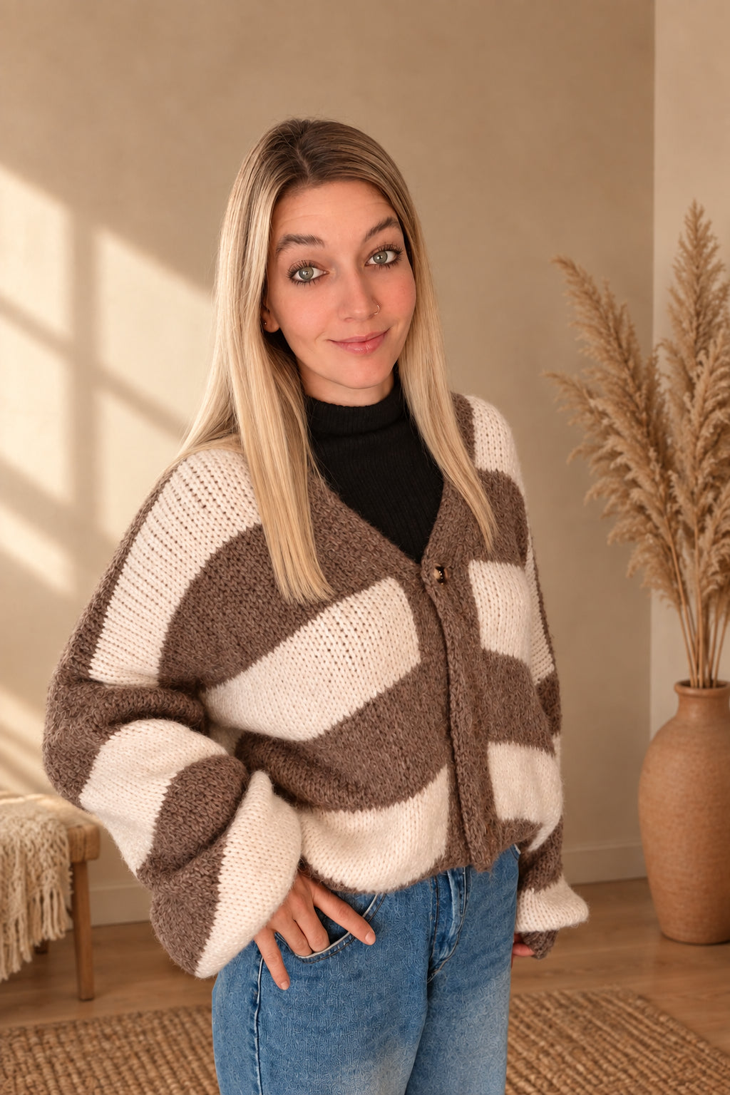 Damen-Strickjacke mit breiten Streifen in Taupe-Creme und Knöpfen, am lächelnden Model mit Händen in den Jeanstaschen.