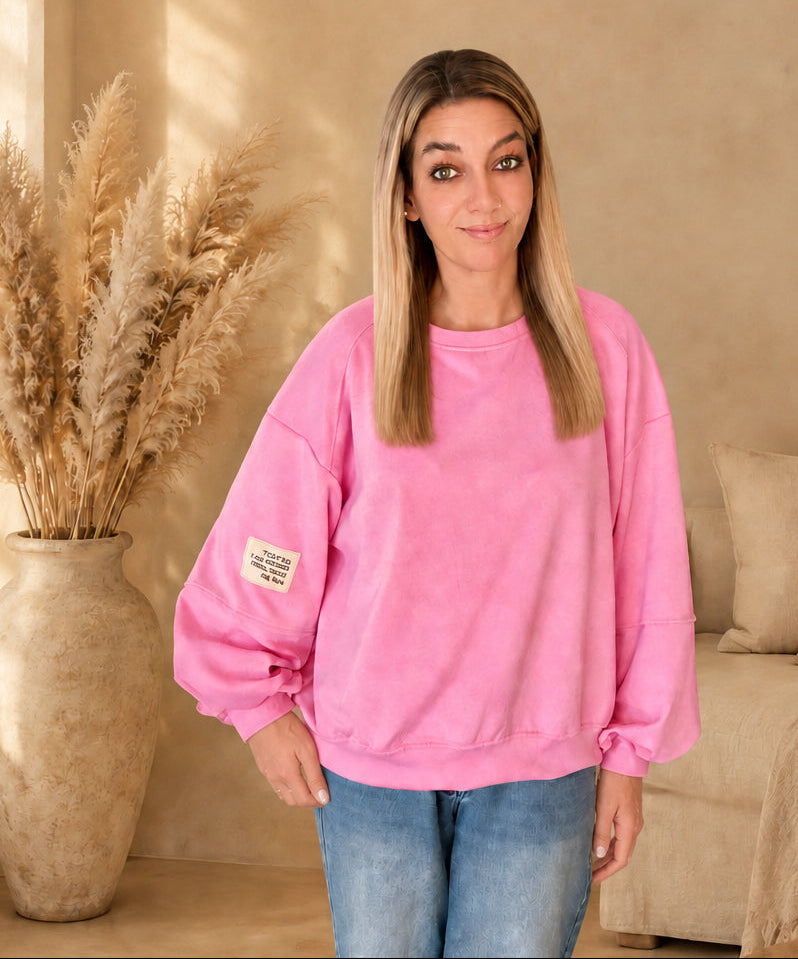 Pinkes Damen-Sweatshirt mit Rundhalsausschnitt, weiten langen Ärmeln und hellem Ärmelpatch, locker über einer blauen Jeans getragen.