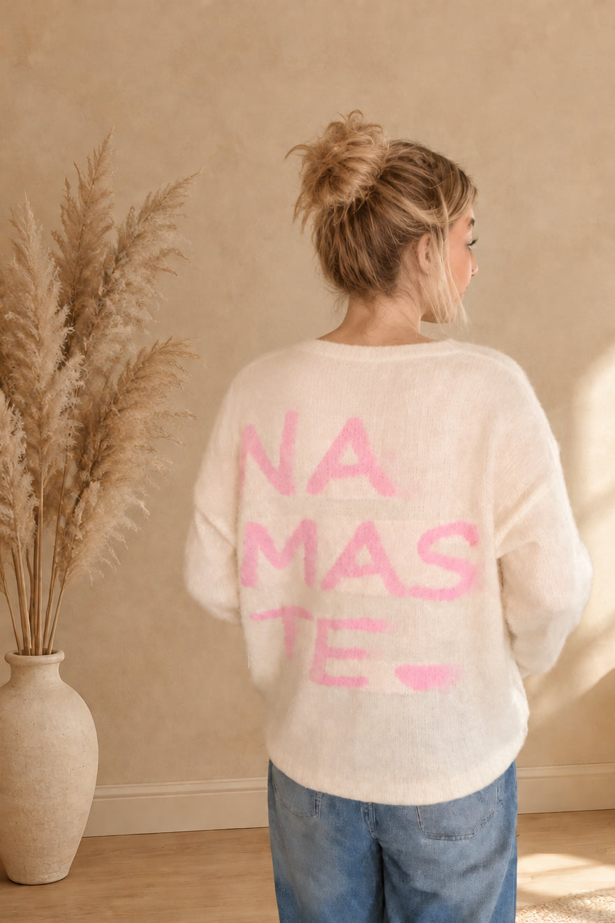 Rückansicht des cremeweißen Strickpullovers mit großem rosa Namasté-Schriftzug und Herz, am Model mit Dutt.