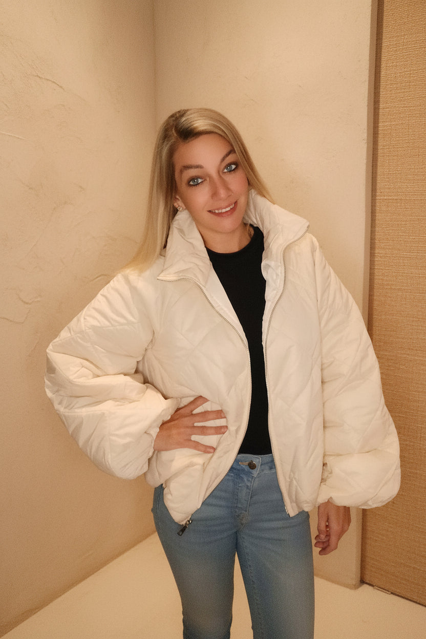 Frau in weißer Steppjacke aus glänzendem Material und hellblauen Jeans im Boho-Luxe Stil.
