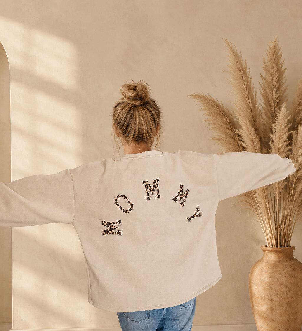 Cremefarbenes Oversize-Sweatshirt mit MOMMY-Schriftzug im Leomuster, Rückansicht mit ausgestreckten Armen.