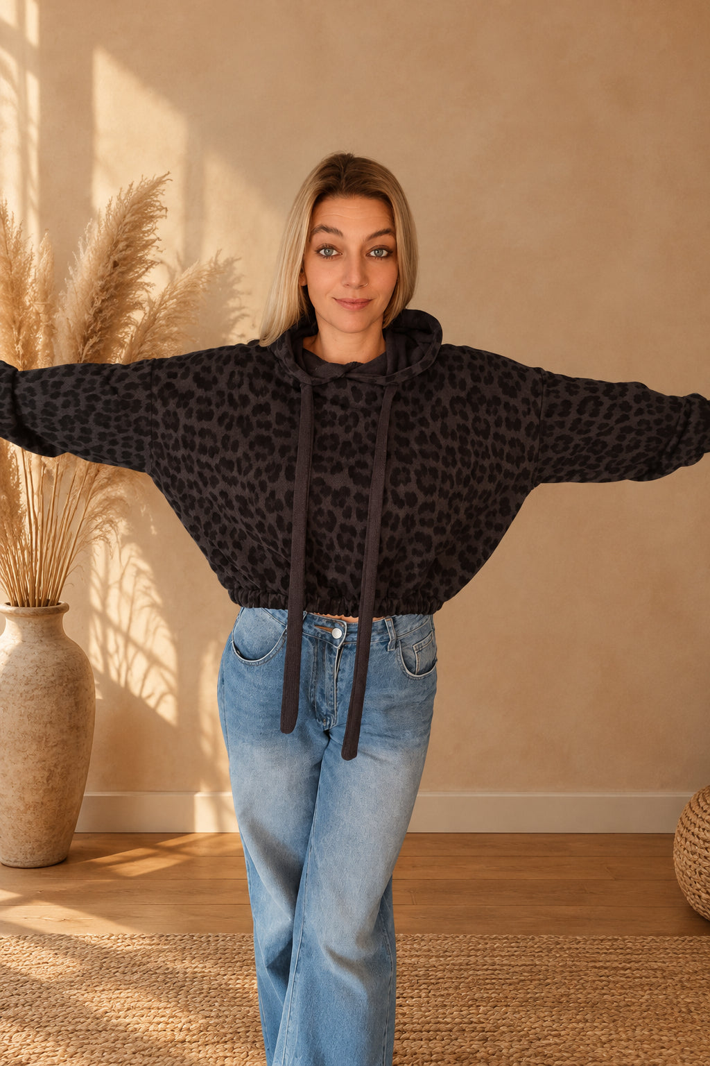 Damen-Leo-Hoodie mit Kapuze, breiten Bindebändern und gerafften Ärmelabschlüssen, zur Jeans mit einer Hand in der Hosentasche getragen.