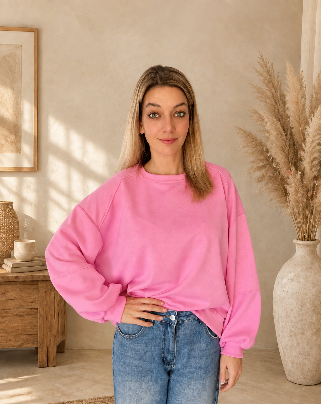 Pinkes Damen-Sweatshirt mit Rundhalsausschnitt und weiten Ärmeln, vorne in eine blaue Jeans gesteckt, eine Hand an der Hüfte.