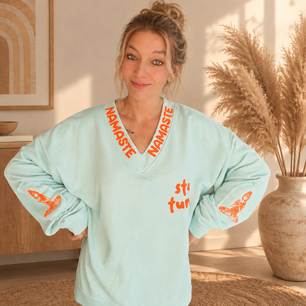 Mintfarbener Damenpullover mit orangefarbenen Motiven auf beiden Ärmeln, Detailansicht am Model
