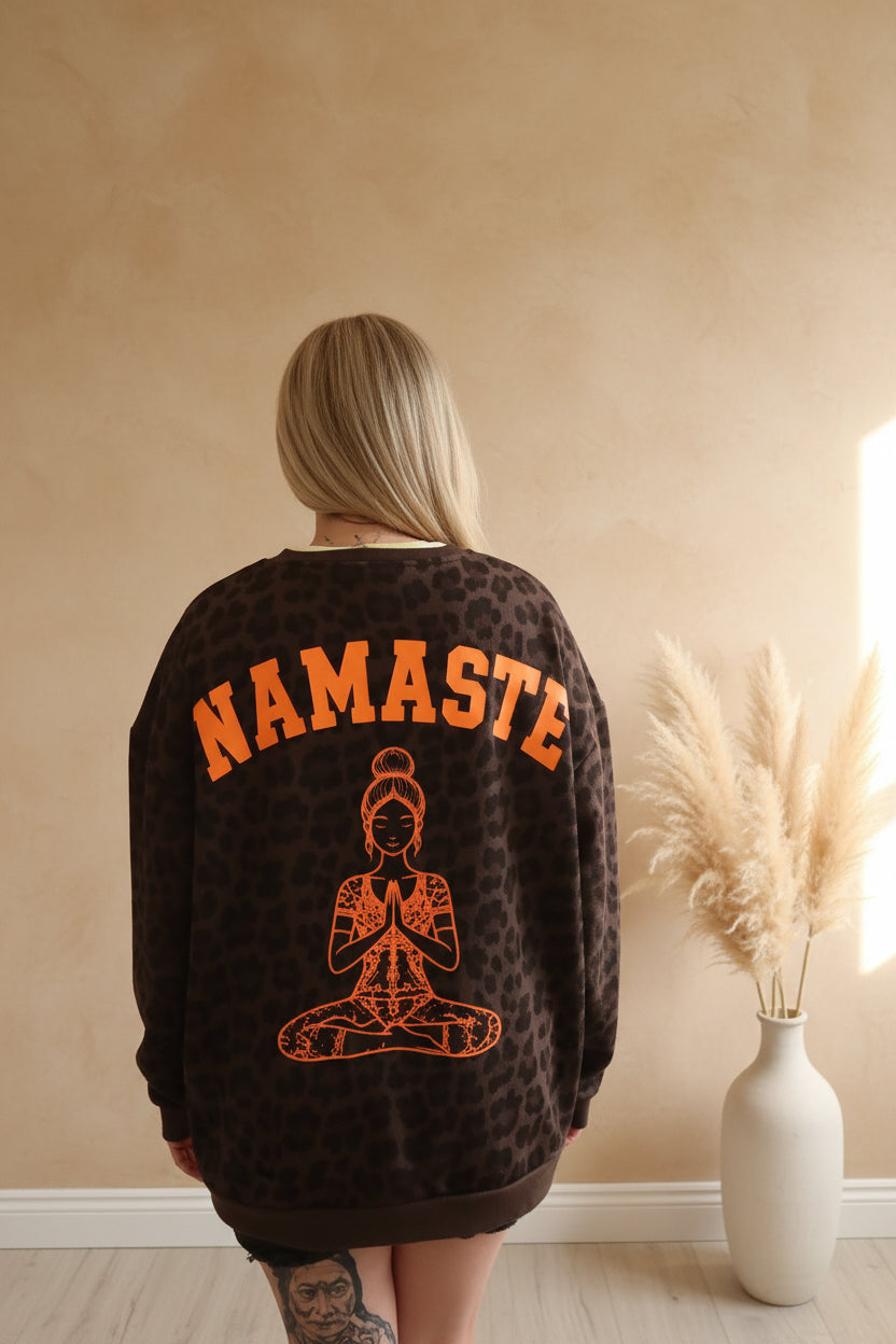 Namasté Oversize Sweater Leo – lässige Pose neonorangem Namasté-Print, warmes Licht