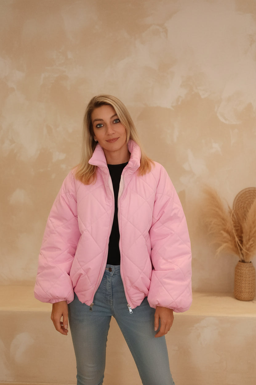 Frau in einer gesteppten, rosa Boho-Luxe Steppjacke aus glänzendem Material und hellblauen Jeans.