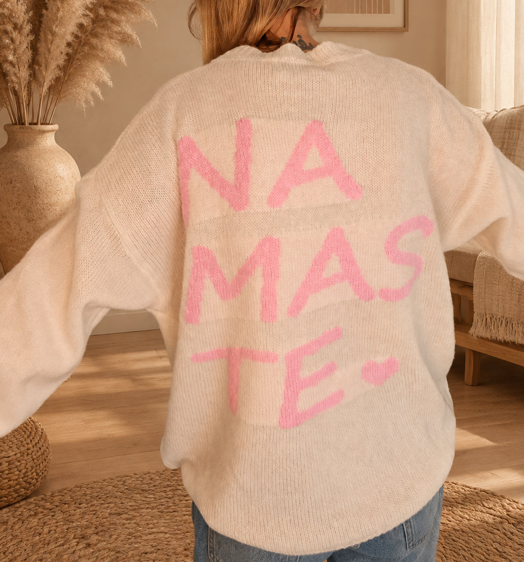 Nahaufnahme der Rückseite des cremeweißen Strickpullovers mit großem rosa Namasté-Schriftzug und Herz.