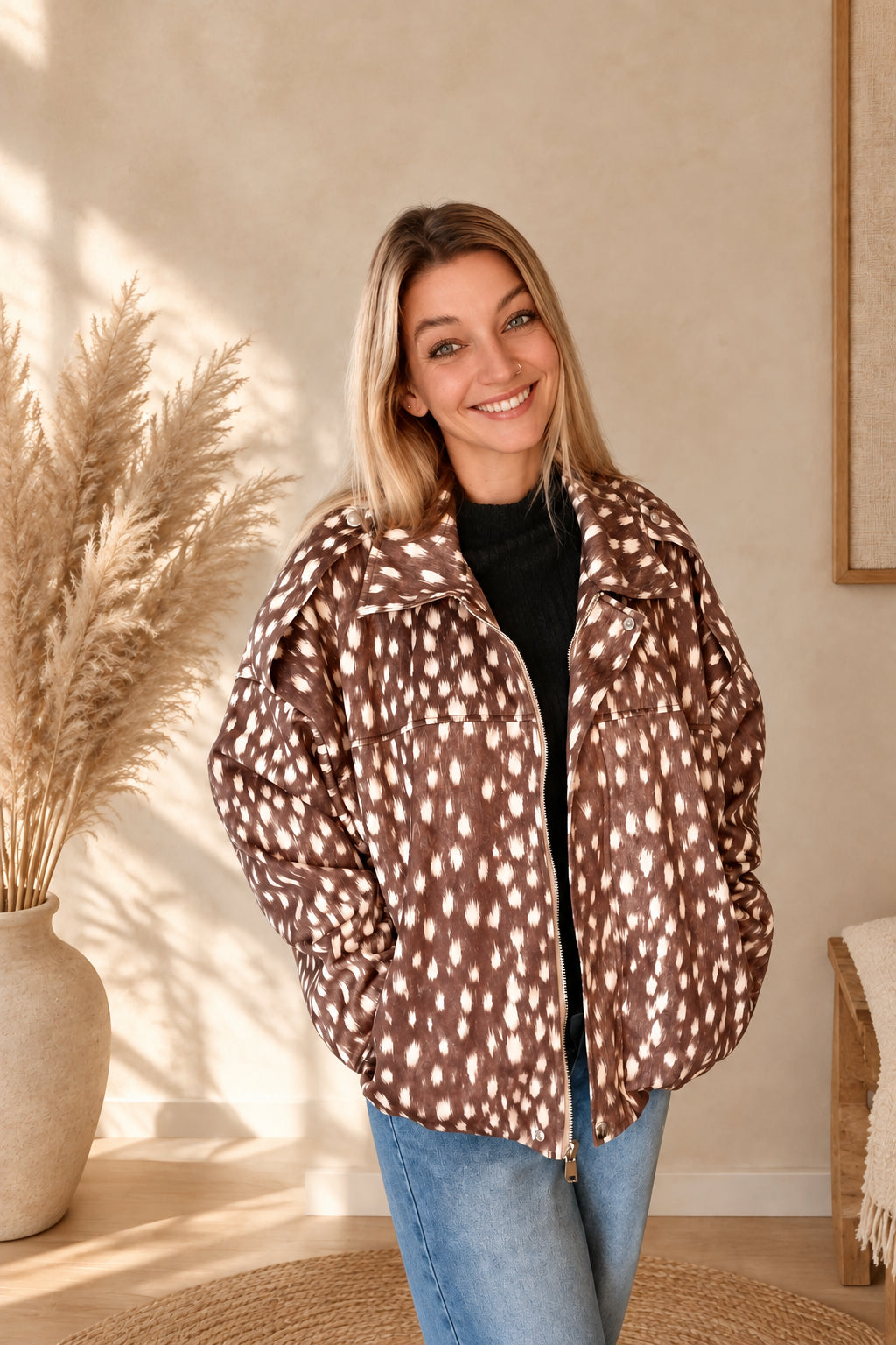 Braune Damenjacke mit cremefarbenem Muster und Reißverschluss, offen am lächelnden Model mit Händen in den Taschen.