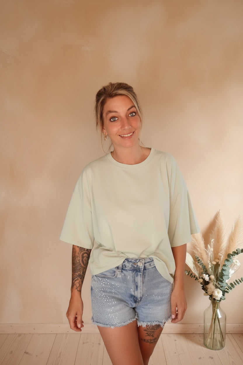 Mintgrünes Oversize T-Shirt Self Love, geknotet getragen, Boho-Styling mit Jeans-Shorts, lächelnde Frau