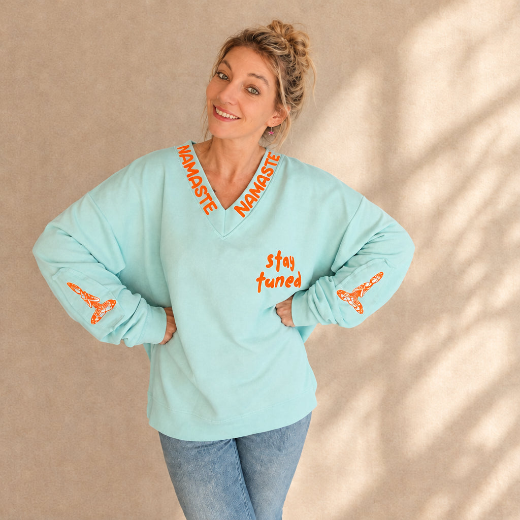 Mintfarbener Damenpullover mit V-Ausschnitt, orangefarbenen Schriftzügen und Ärmelprints, lockere Frontansicht