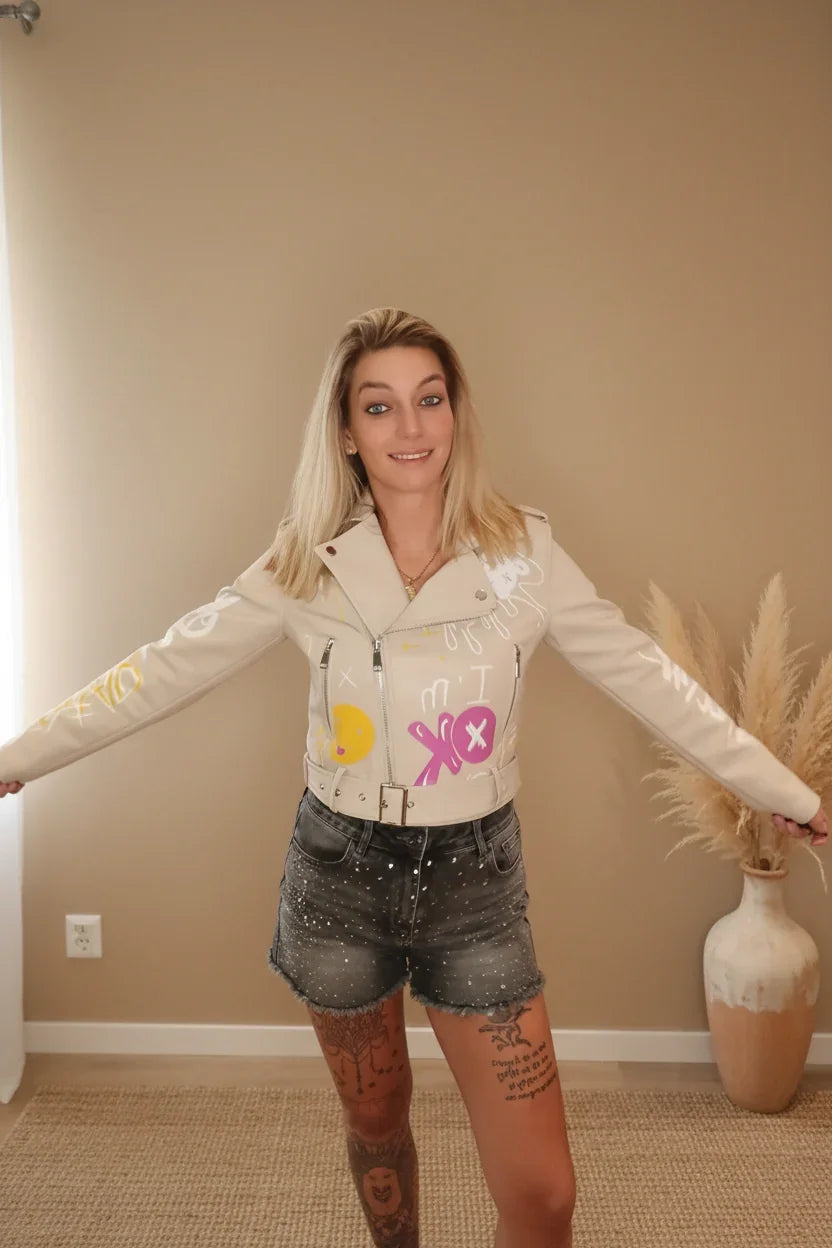 Frau in beiger Lederjacke mit farbigen Grafiken und kurzen Denim-Shorts im Boho-Luxe Stil.
