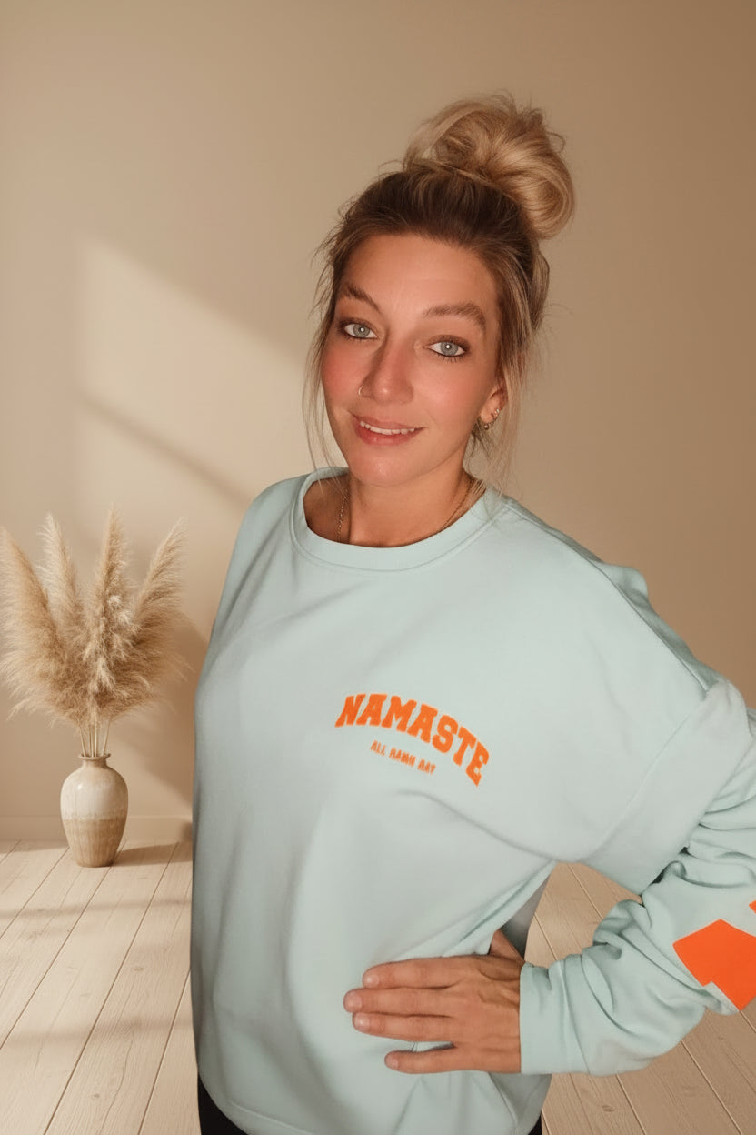 Namaste Sweatshirt Pastellblau – Seitenansicht mit orangem Ärmelprint