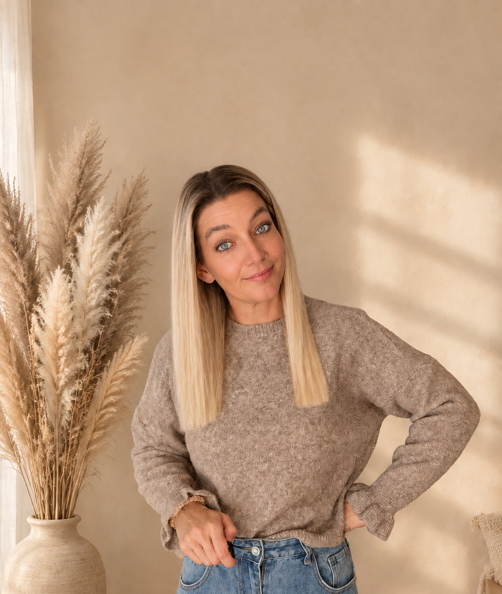 Taupefarbener Damenpullover am Model mit einer Hand an der Hüfte und der anderen am Jeansbund.