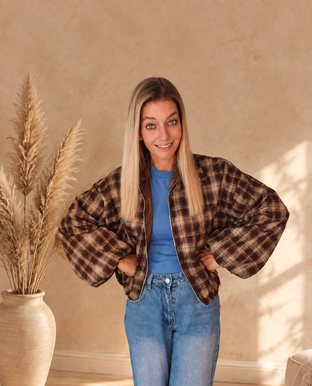 Offene karierte Damenjacke in Dunkelbraun und Beige mit voluminösen Ärmeln, Hände an der Hüfte.