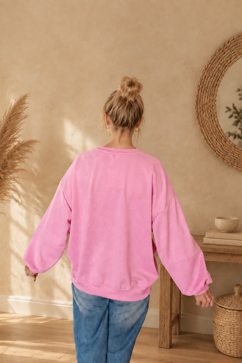 Rückansicht des pinken Damen-Sweatshirts mit lockerem Schnitt und Saumbündchen, am Model mit Dutt und leicht ausgestreckten Armen.